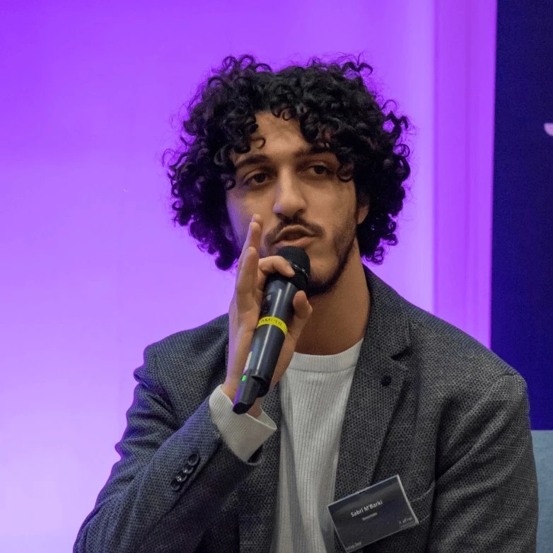 Sabri en intervention, micro en main, sur fond violet